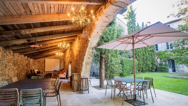 An outdoor patio with stone walls, wooden beams, and a table with chairs.
