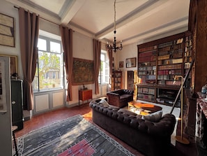 Ein Wohnzimmer mit einer großen Bücherwand, einem Sofa, einem Teppich und einer Kronleuchter.