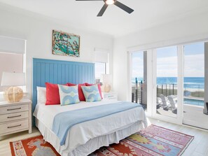 A bedroom with a large bed, a ceiling fan, a nightstand, a lamp, a painting, and a view of the ocean through a sliding door. - Viviana #8 by Southern Vacation Rentals (Pensacola)