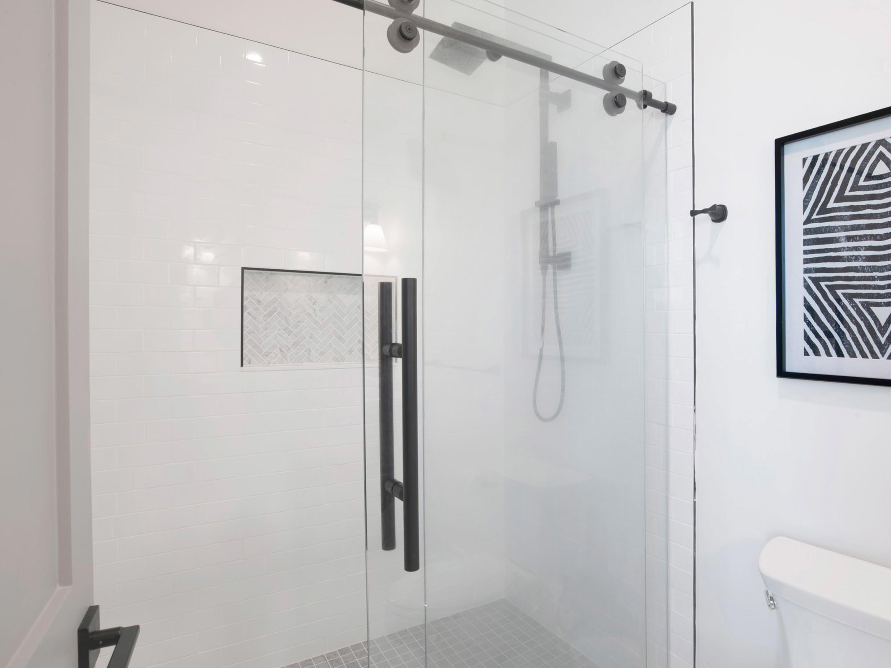 A modern bathroom with a glass shower enclosure, a white toilet, and a framed abstract artwork on the wall.