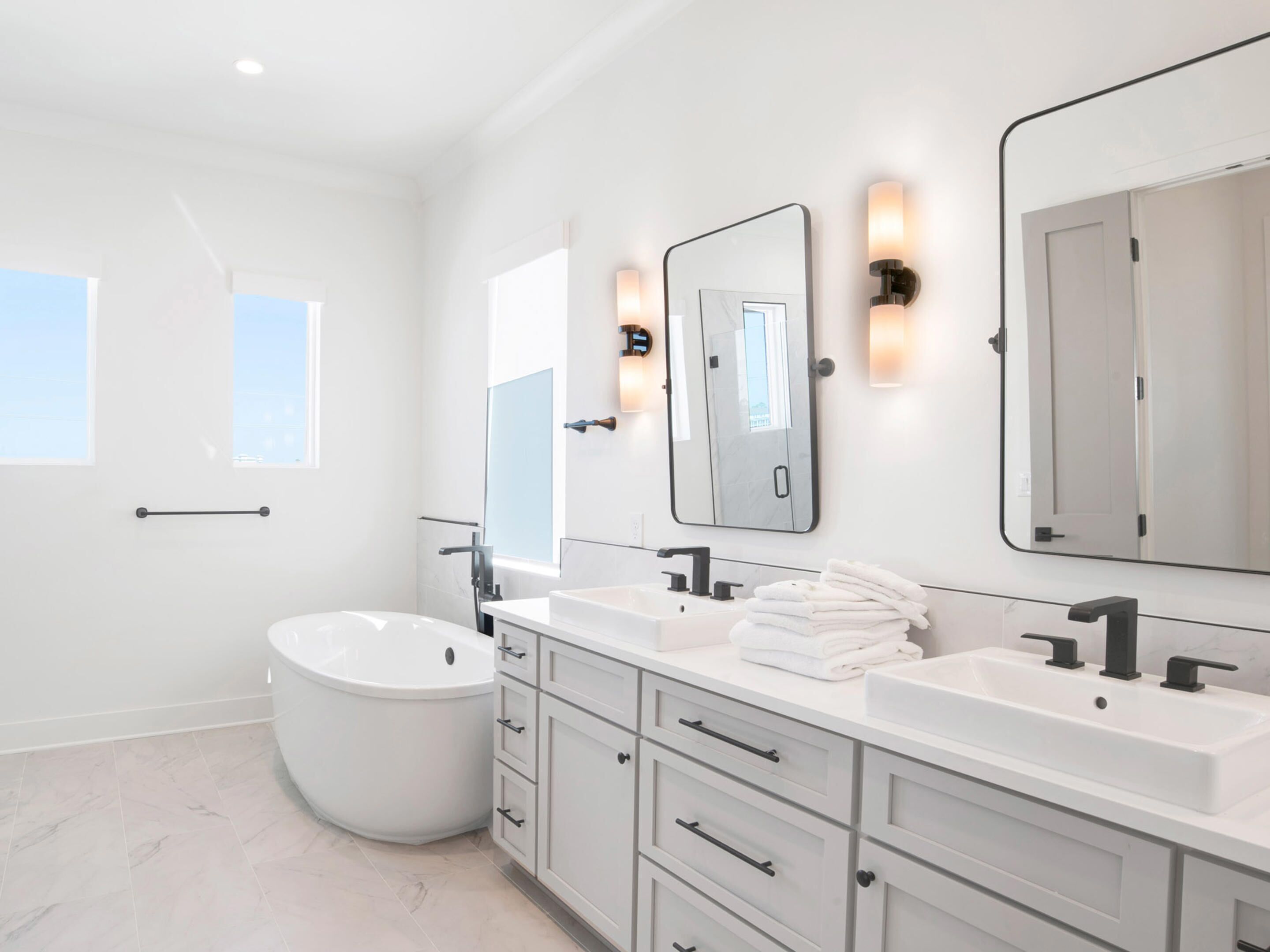 A modern bathroom with a freestanding bathtub, two sinks, and a large mirror.