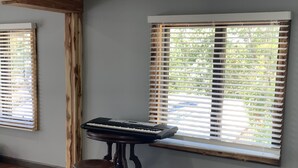 A room with a piano on a wooden stand, a stool, and a window with blinds. - 1. Apartment with hot tub and fireplace (Rockaway Beach)