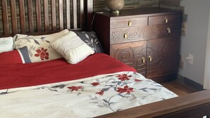 A bedroom with a wooden headboard, a bed with floral bedding, a dresser with decorative panels, and a lamp on the dresser. - 1. Apartment with hot tub and fireplace (Rockaway Beach)