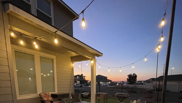 An outdoor patio area with string lights, a covered seating area, and a fire pit. - New, 3 Bedroom Home Centrally Located in Moses Lake with Room for all Your Toys! (Moses Lake)