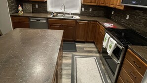 A modern kitchen with wooden cabinets, a stainless steel sink, a microwave, and a stove. - New, 3 Bedroom Home Centrally Located in Moses Lake with Room for all Your Toys! (Moses Lake)