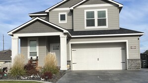 A two-story house with a garage, a driveway, and a well-maintained lawn. - New, 3 Bedroom Home Centrally Located in Moses Lake with Room for all Your Toys! (Moses Lake)