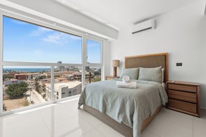 Un dormitorio moderno con un ventanal grande, una cama con cabecera de madera, una mesita de noche y vistas a la ciudad.