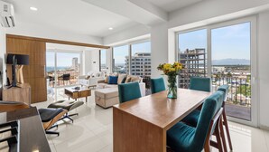 A modern living room with a dining area, large windows, and a view of the city. - MONYXBNB HOTEL (Puerto Vallarta)