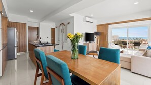 A modern apartment with a kitchen, dining area, and living room. It features a large window with a view of the city and a balcony. - MONYXBNB HOTEL (Puerto Vallarta)
