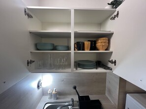 Compact kitchen with minimalist design, featuring two shelves for kitchenware and a small sink with faucet.