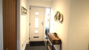 Un couloir avec une porte en bois, une porte blanche, un banc avec une plante et un miroir fixé au mur.