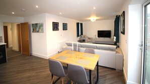 Un salon moderne avec un coin repas, un canapé, un téléviseur et une cuisine en arrière-plan.