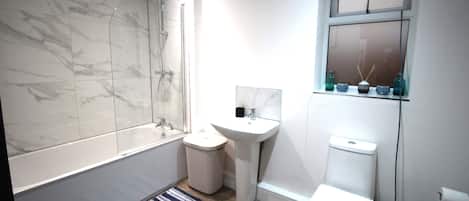 A modern bathroom with a marble shower, a pedestal sink, a toilet, and a small window with decorative items.