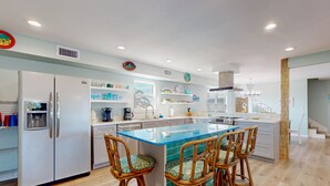 A modern kitchen with a central island, bar stools, and a refrigerator. - Wet Bar, Outdoor Games, Gulf Views, Pet Friendly (Port Aransas)