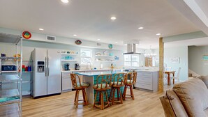 A modern kitchen with a central island, bar stools, and a dining area with a sofa. - Wet Bar, Outdoor Games, Gulf Views, Pet Friendly (Port Aransas)
