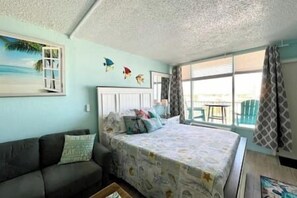 A bedroom with a bed, a sofa, a window with curtains, and a view of the outdoors.