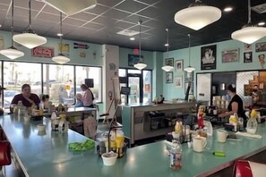 A restaurant interior with a counter, seating area, and various kitchen appliances.