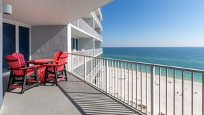 Un balcone con vista sulla spiaggia, sedie rosse e un corrimano bianco.