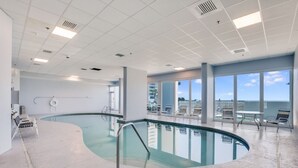 Una piscina interna con pareti in vetro trasparente, una zona solarium con lettini e vista sul cielo attraverso ampie finestre.