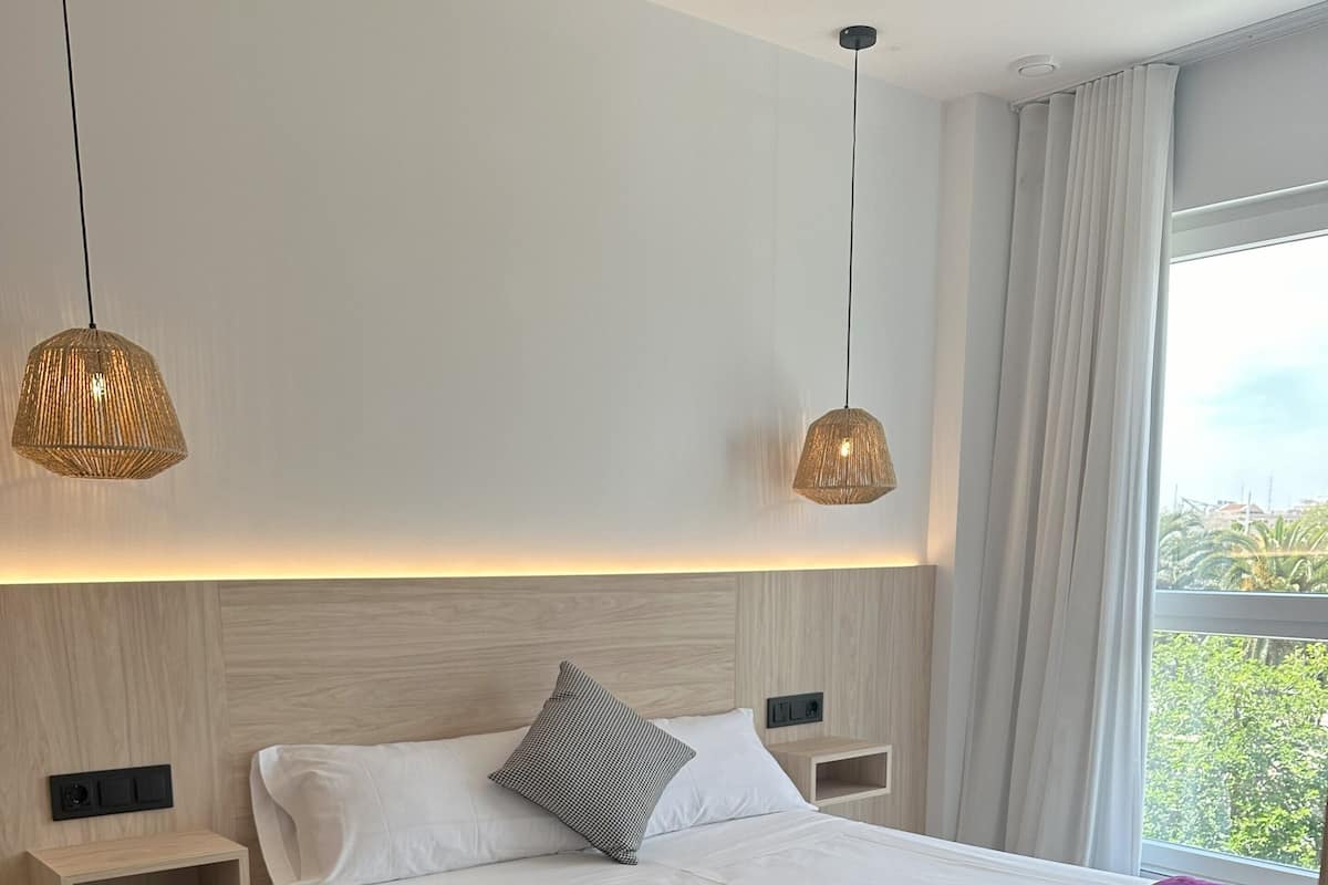 Une chambre à coucher moderne avec un lit en bois, une literie blanche, un plaid violet et deux tables de chevet avec des lampes.