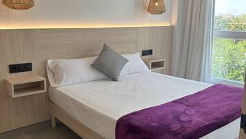 A modern bedroom with a wooden bed, white bedding, a purple throw blanket, and two bedside tables with lamps.