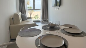 Un comedor con una mesa redonda preparada para dos personas, un sofá con cojines y un amplio ventanal con cortinas.