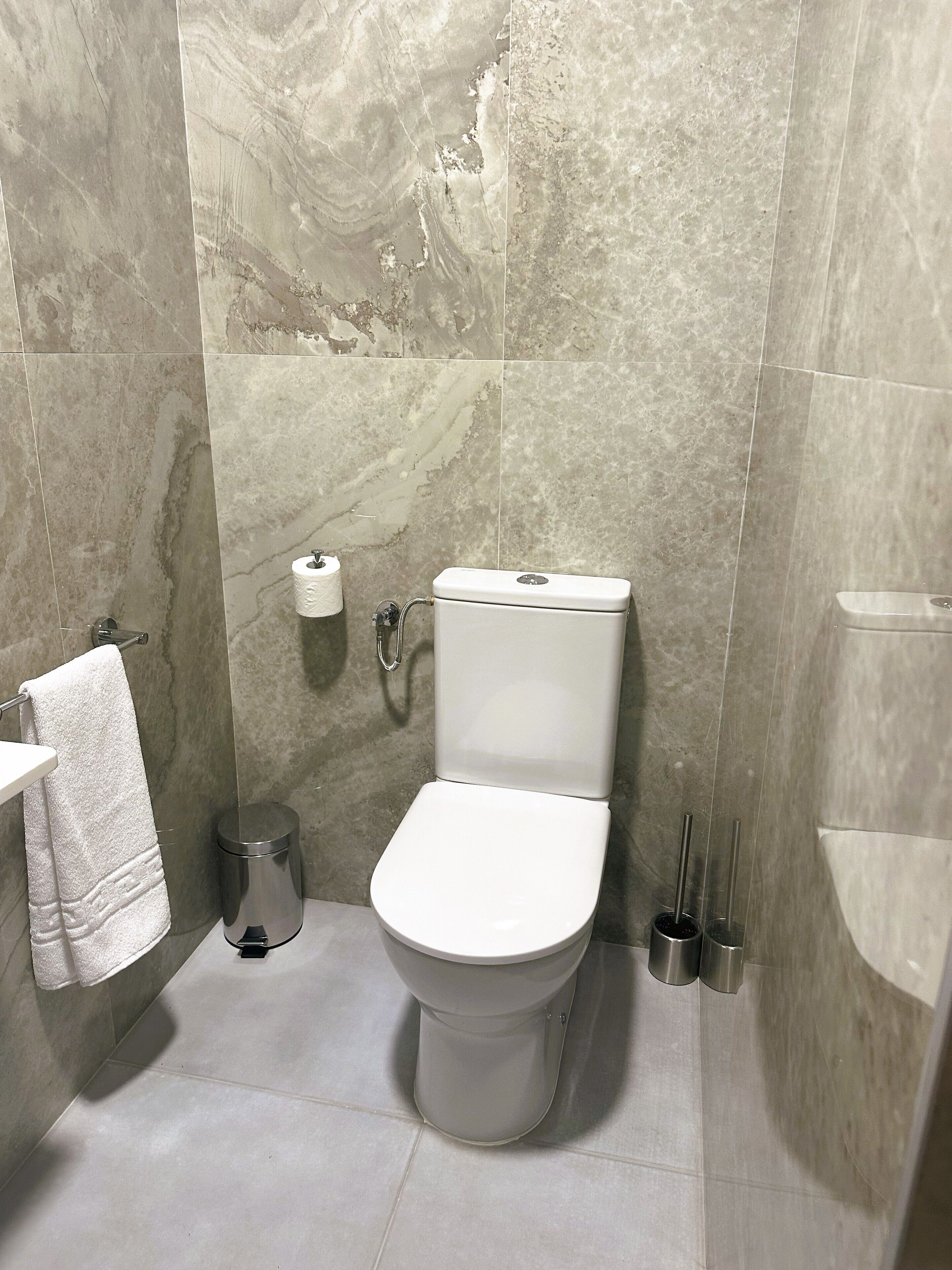 Un baño moderno con inodoro, paredes de mármol, un perchero y un cubo de basura.
