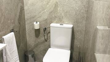 Un baño moderno con inodoro, paredes de mármol, un perchero y un cubo de basura.