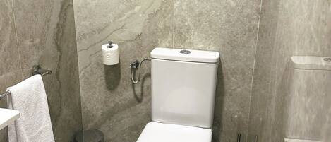 A modern bathroom with a toilet, marble walls, a towel rack, and a trash can.