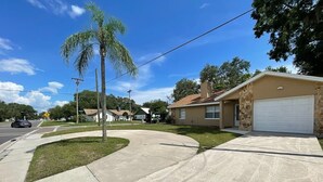 A residential street with a house featuring a garage, a driveway, and a well-maintained lawn.