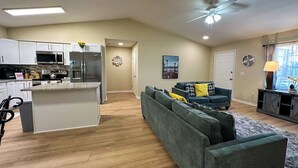 A modern kitchen with white cabinets, a central island, and a dining area with a blue sofa and a lamp.