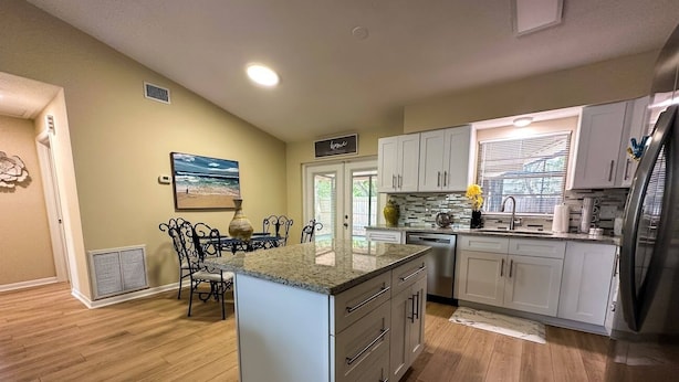 A modern kitchen with white cabinets, a granite countertop island, and a dining area with a metal chair and table.