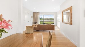 A modern living room with a wooden dining table, a sofa, and a large window with a view of a bridge.