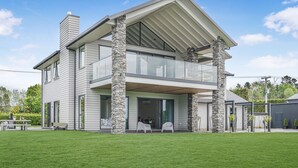 A modern two-story house with a balcony, stone pillars, and a well-maintained lawn.