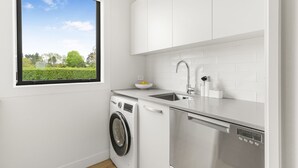 A modern kitchen with a washing machine, dishwasher, and a window with a view of greenery.