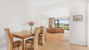 A dining area with a wooden table and chairs, a vase with flowers, and a view of a balcony with a sofa.
