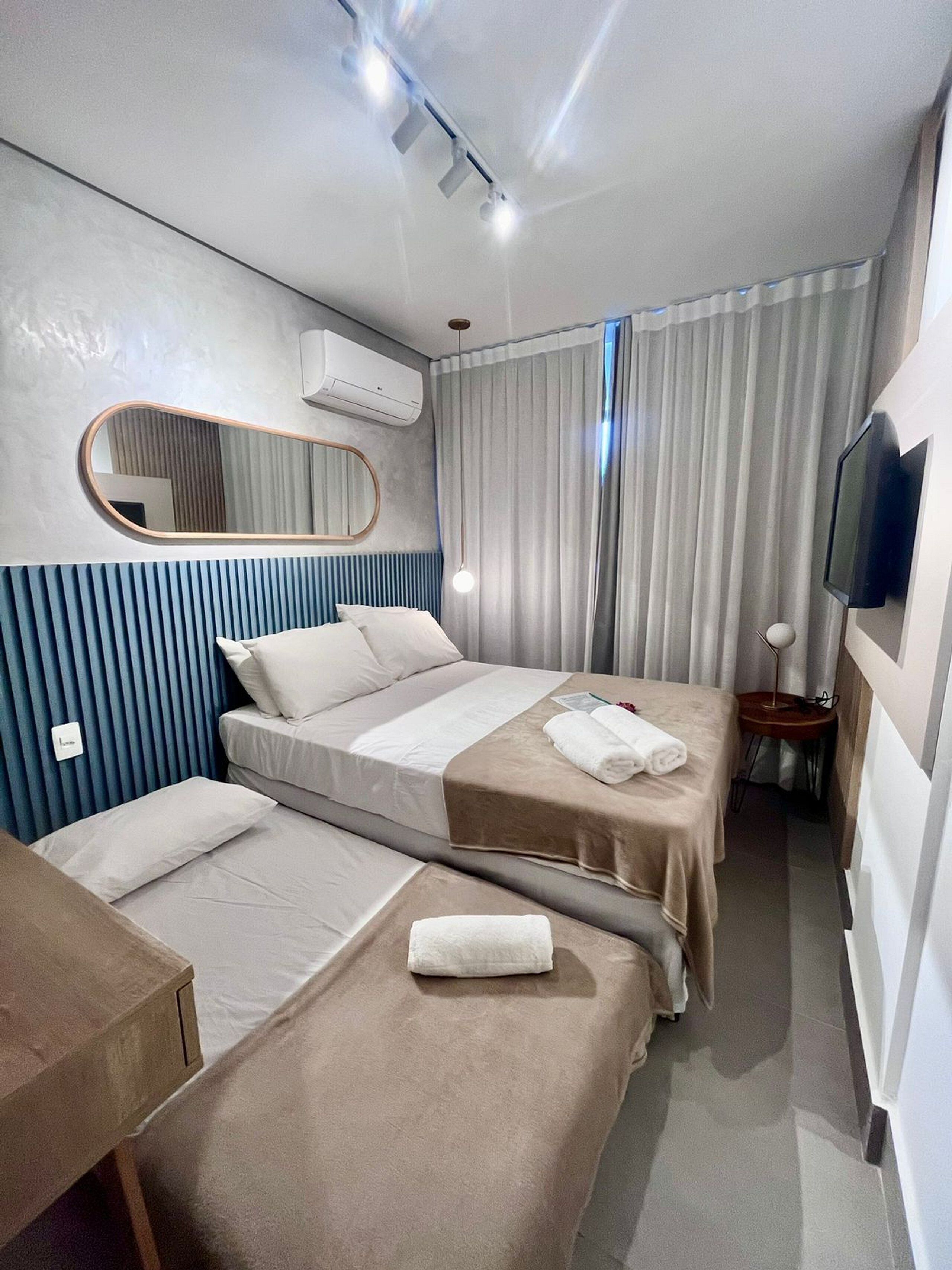 A hotel room with two beds, a TV, a mirror, and an air conditioning unit.