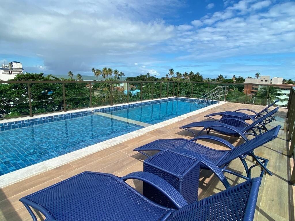 A swimming pool with lounge chairs and a view of the ocean and palm trees.