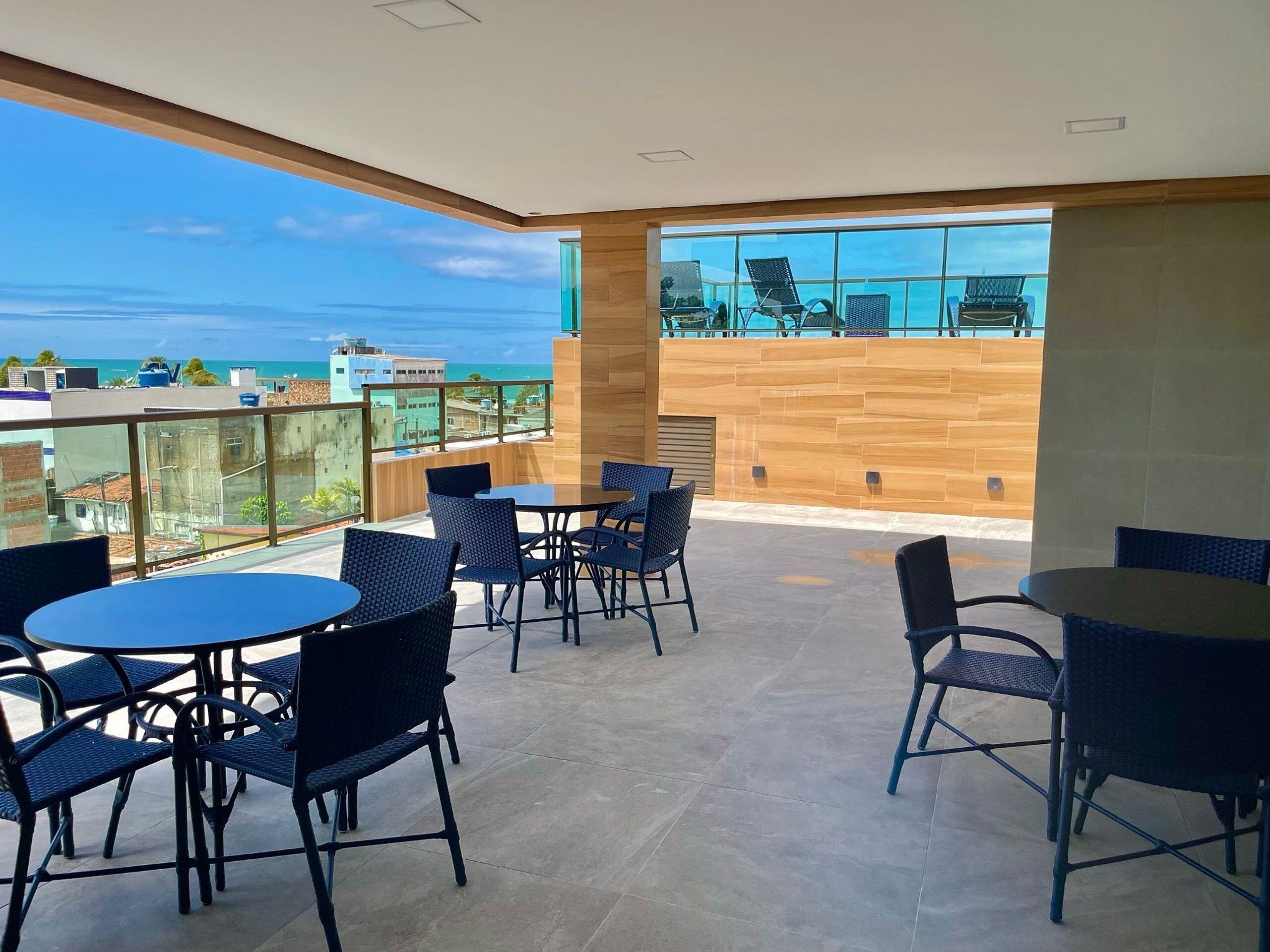 A rooftop terrace with tables and chairs, offering a view of the cityscape and ocean.