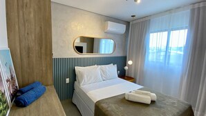 Quarto de hotel com cama, mesa de cabeceira com toalhas, espelho e janela com cortinas.