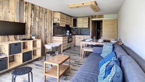 A modern living space with a wooden wall, a flat-screen TV, a sofa, a dining table, and a kitchen area. - Ski-in/ski-out & foot of the slopes, 8th floor, balcony, tv, ski locker, 40m², Les Menuires (Les Menuires)