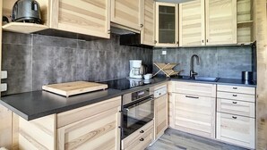 A modern kitchen with wooden cabinetry, a black countertop, and a built-in oven. - Ski-in/ski-out & foot of the slopes, 8th floor, balcony, tv, ski locker, 40m², Les Menuires (Les Menuires)