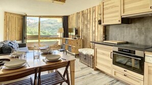 A modern kitchen with wooden cabinets, a dining area with a table set for four, and a large window offering a view of the mountains. - Ski-in/ski-out & foot of the slopes, 8th floor, balcony, tv, ski locker, 40m², Les Menuires (Les Menuires)