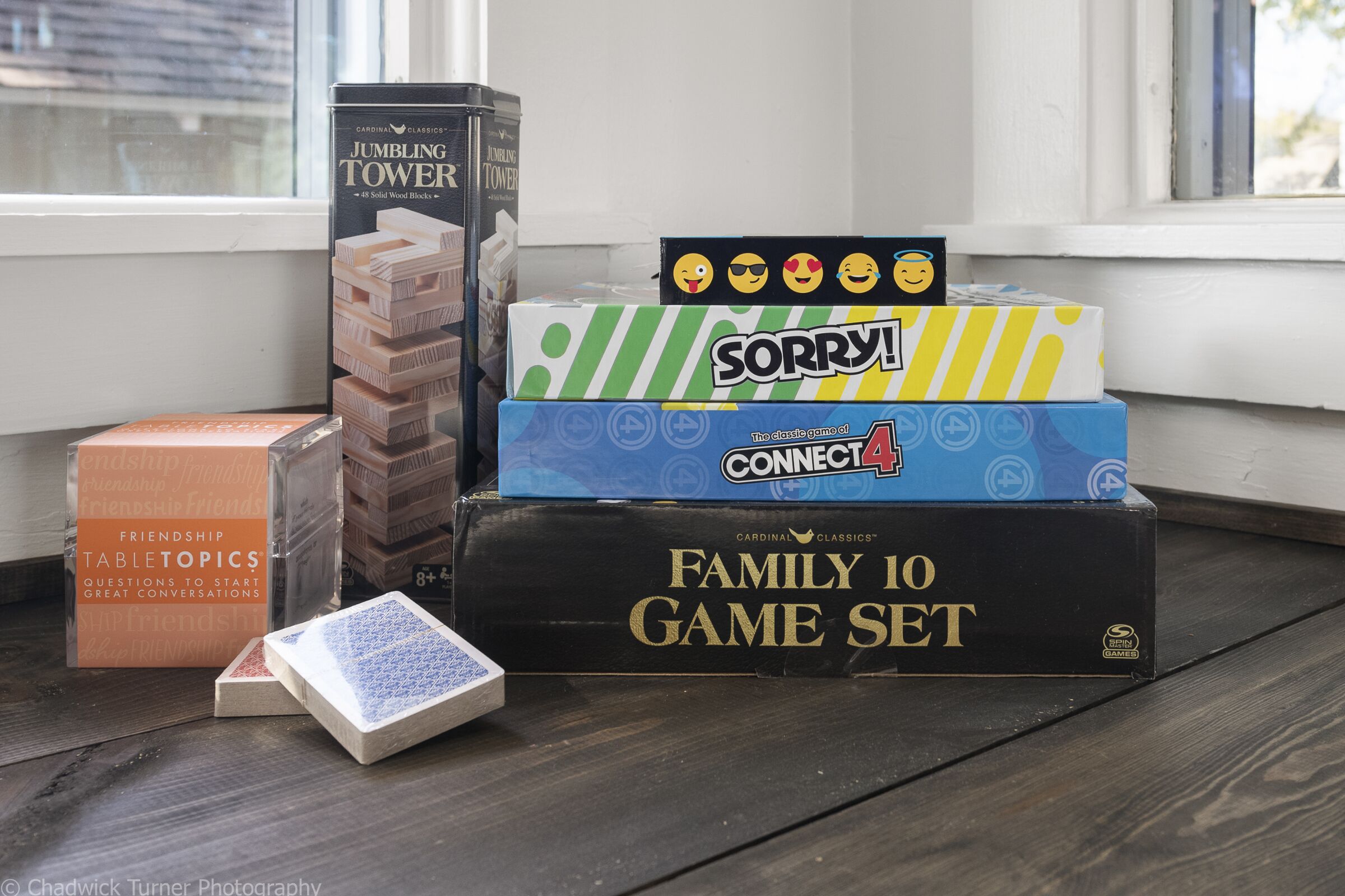 Eine Auswahl Brettspiele, darunter JUMBLING TOWER, SORRY!, CONNECT4 und ein FAMILY 10 SPIELSET, auf einer Holzoberfläche in der Nähe eines Fensters.