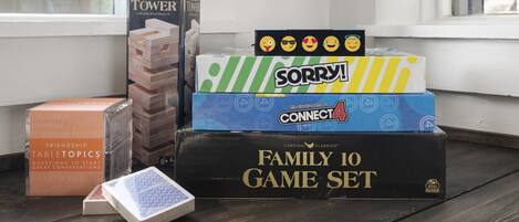 Eine Auswahl Brettspiele, darunter JUMBLING TOWER, SORRY!, CONNECT4 und ein FAMILY 10 SPIELSET, auf einer Holzoberfläche in der Nähe eines Fensters.