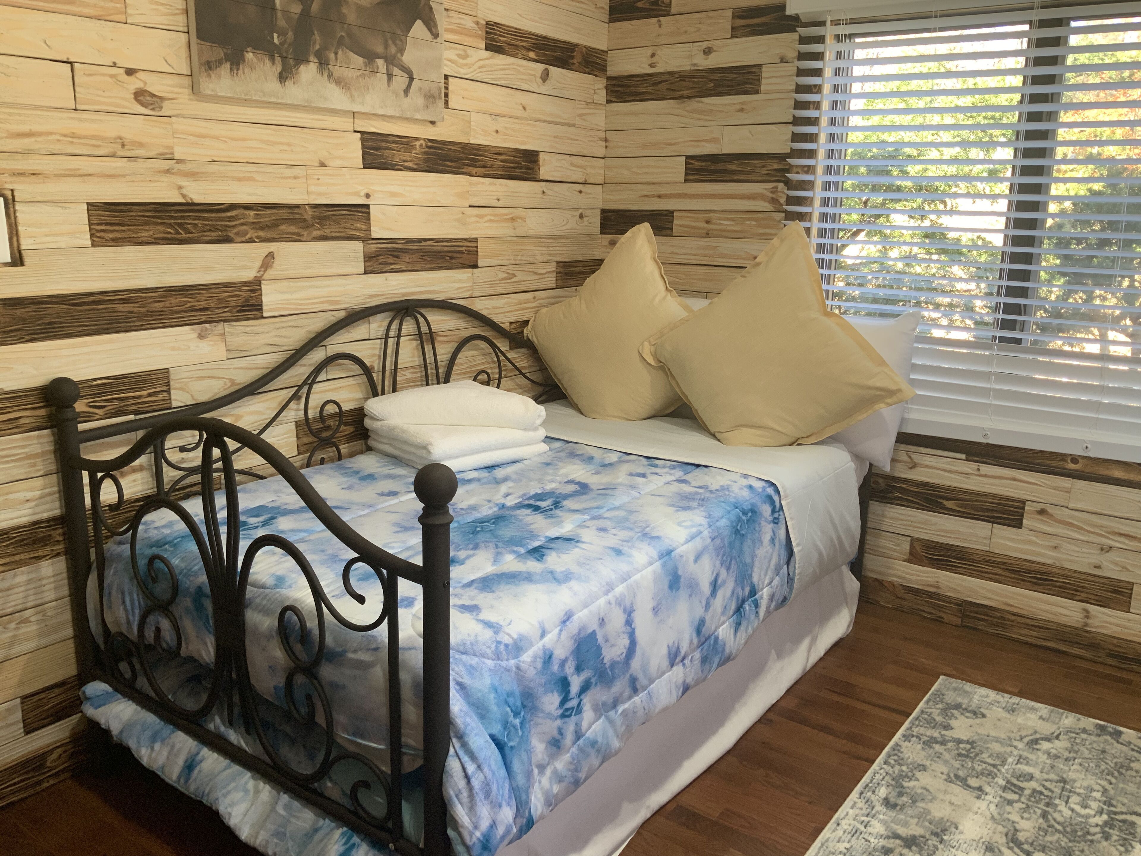 Un dormitorio con cama, paneles de madera en la pared, una ventana con persianas y una alfombra en el suelo.