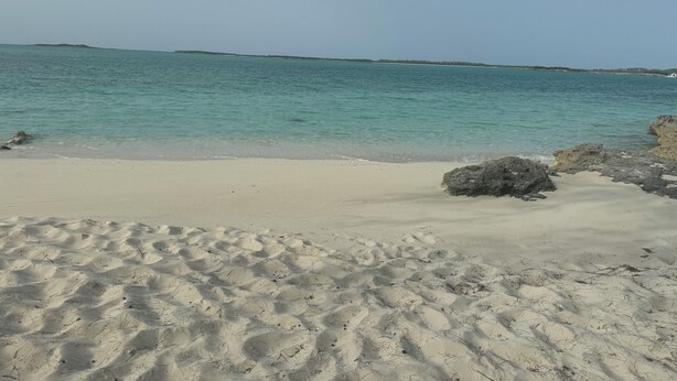 Ein sandiger Strand mit klarem türkisblauem Wasser und weiter Küstenlinie.
