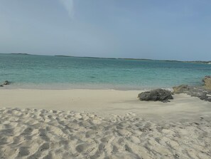 Une plage de sable fin bordée d’une eau turquoise et limpide, avec une terre lointaine à l’horizon.