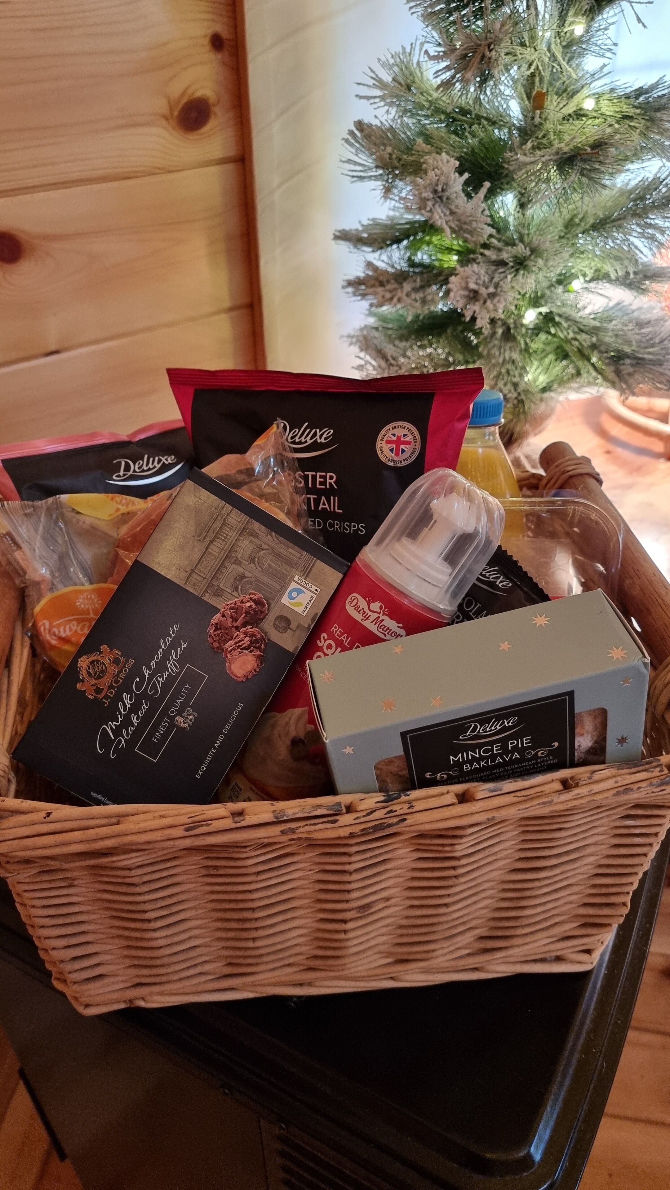 A wicker basket filled with various food items including chocolate truffles, a bottle of juice, and a box of pie.