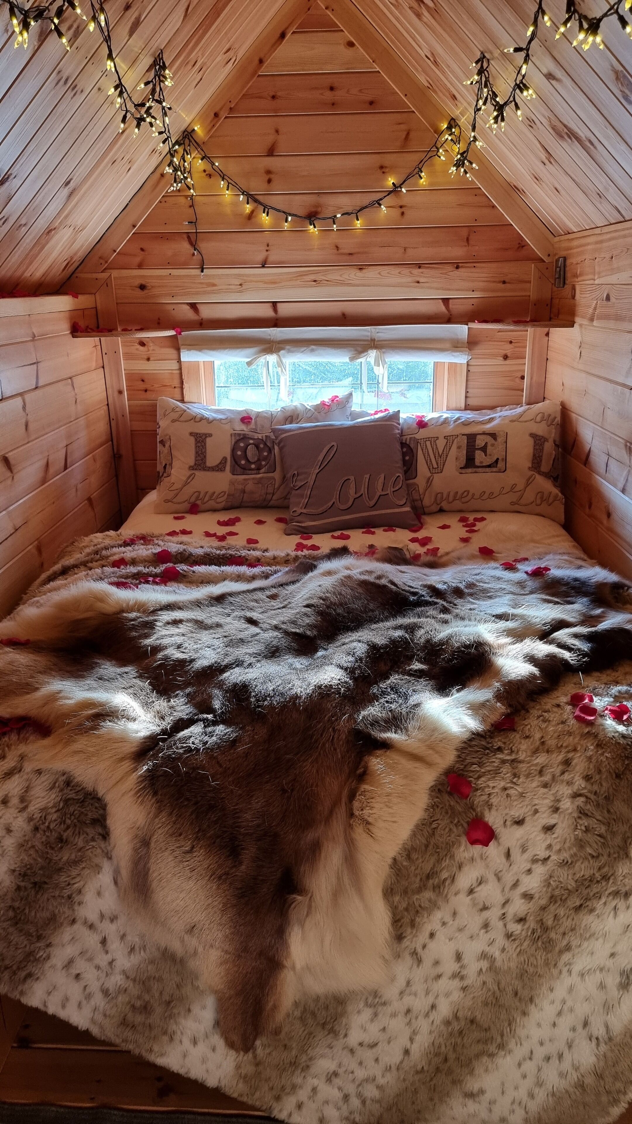 A cozy wooden cabin bedroom with a bed adorned with rose petals and a fluffy blanket.